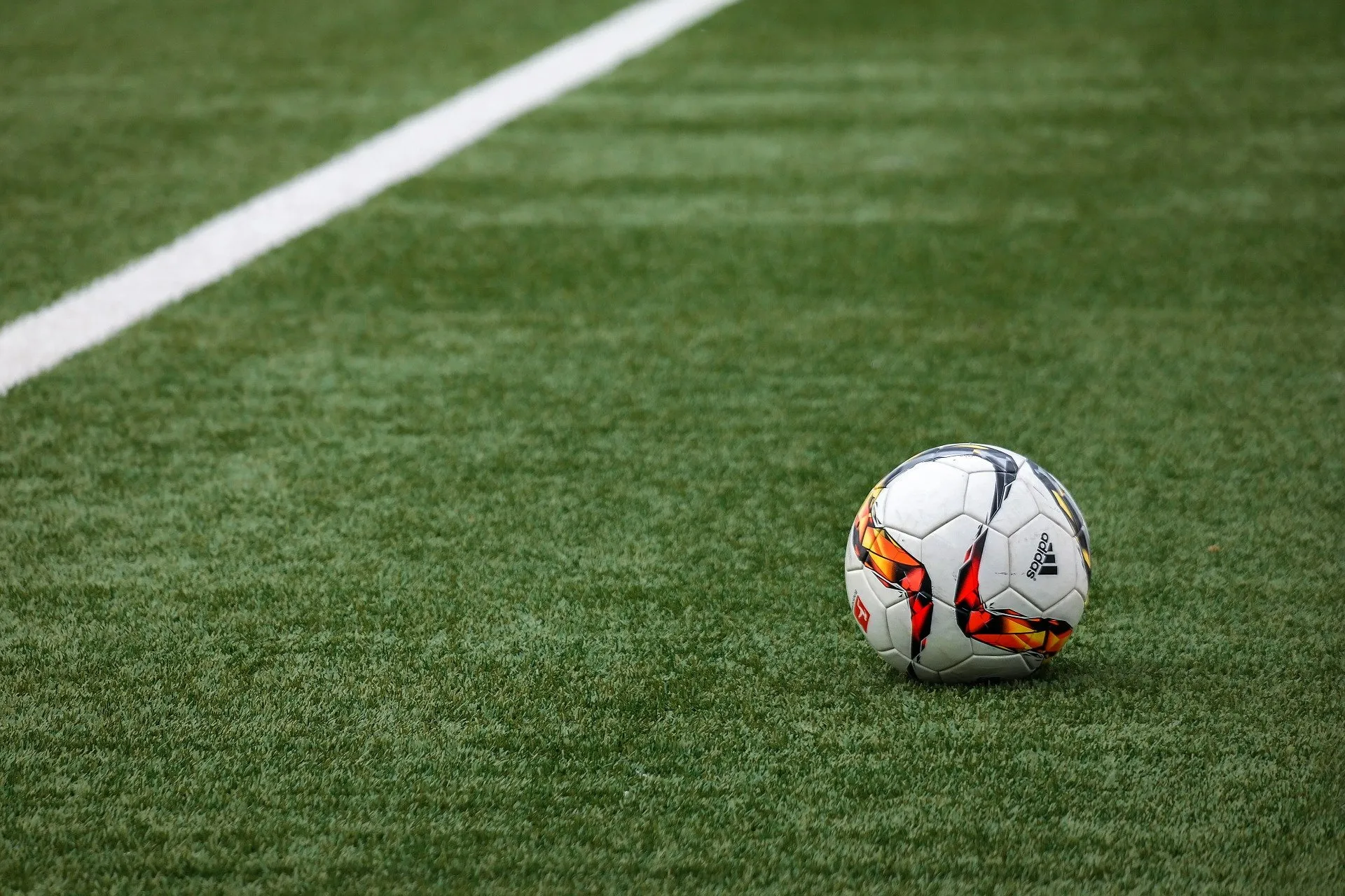 A soccer ball with red and black patterns rests on a lush field of custom putting greens, near a white sideline, under the bright daylight sky in Ahwatukee AZ.